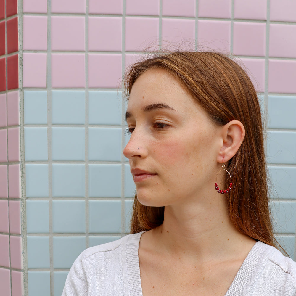 gold macrame hoop earrings with garnet beads worn on a model
