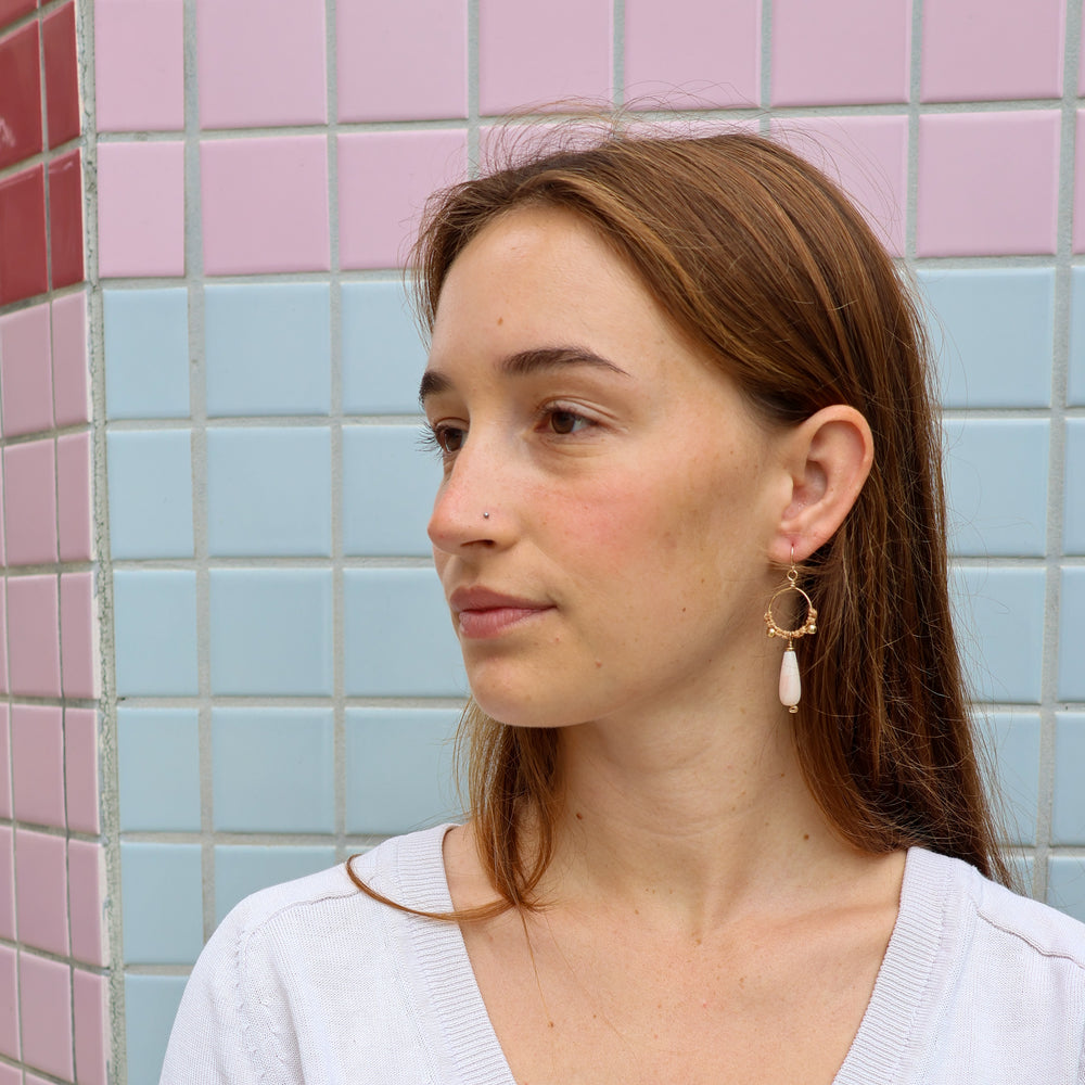 gold macrame hoop earrings with pink opal teardrop beads worn on a model