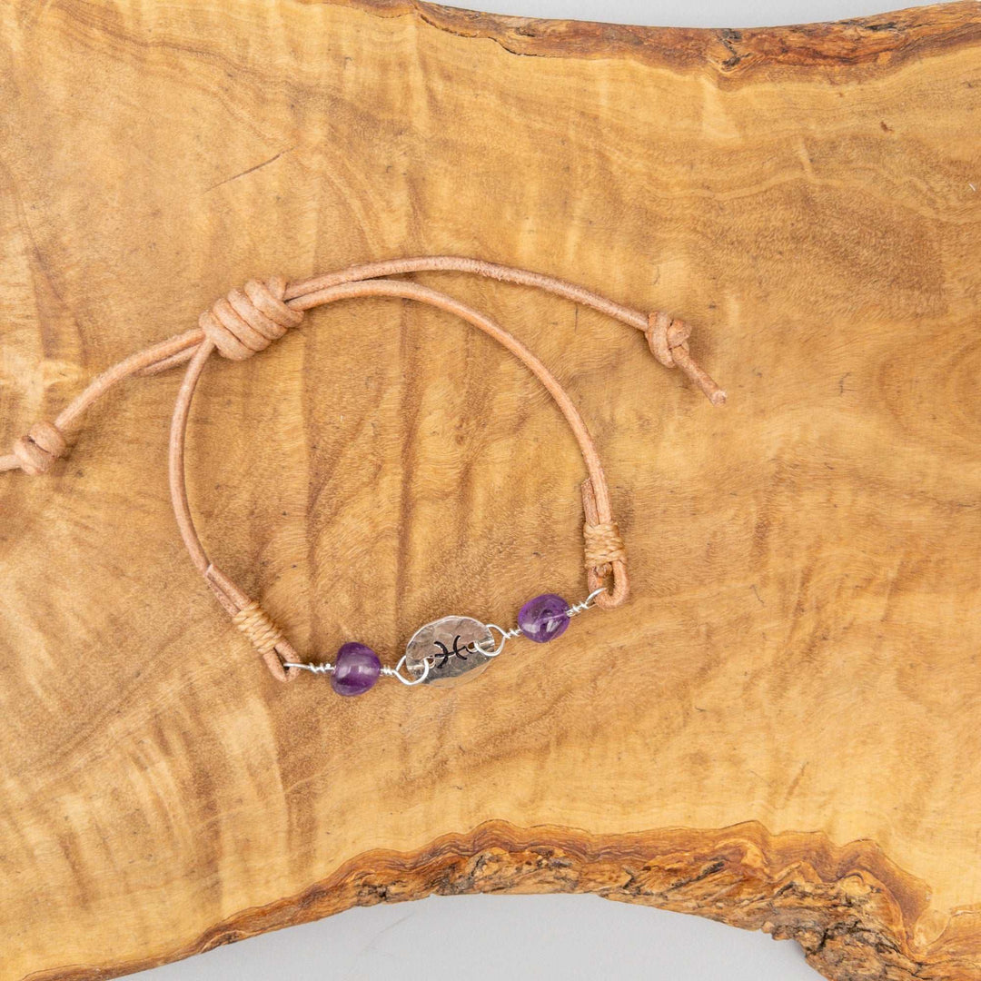 Pisces bracelet with amethyst beads. Hand stamped sterling silver and natural leather. Shown on a wood background