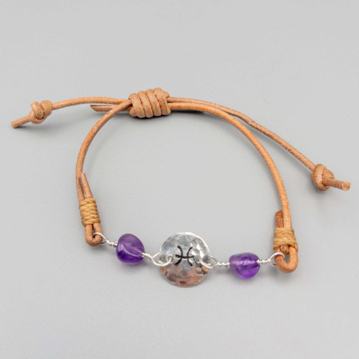 Pisces bracelet with amethyst beads. Hand stamped sterling silver and natural leather. Shown on a gray background.