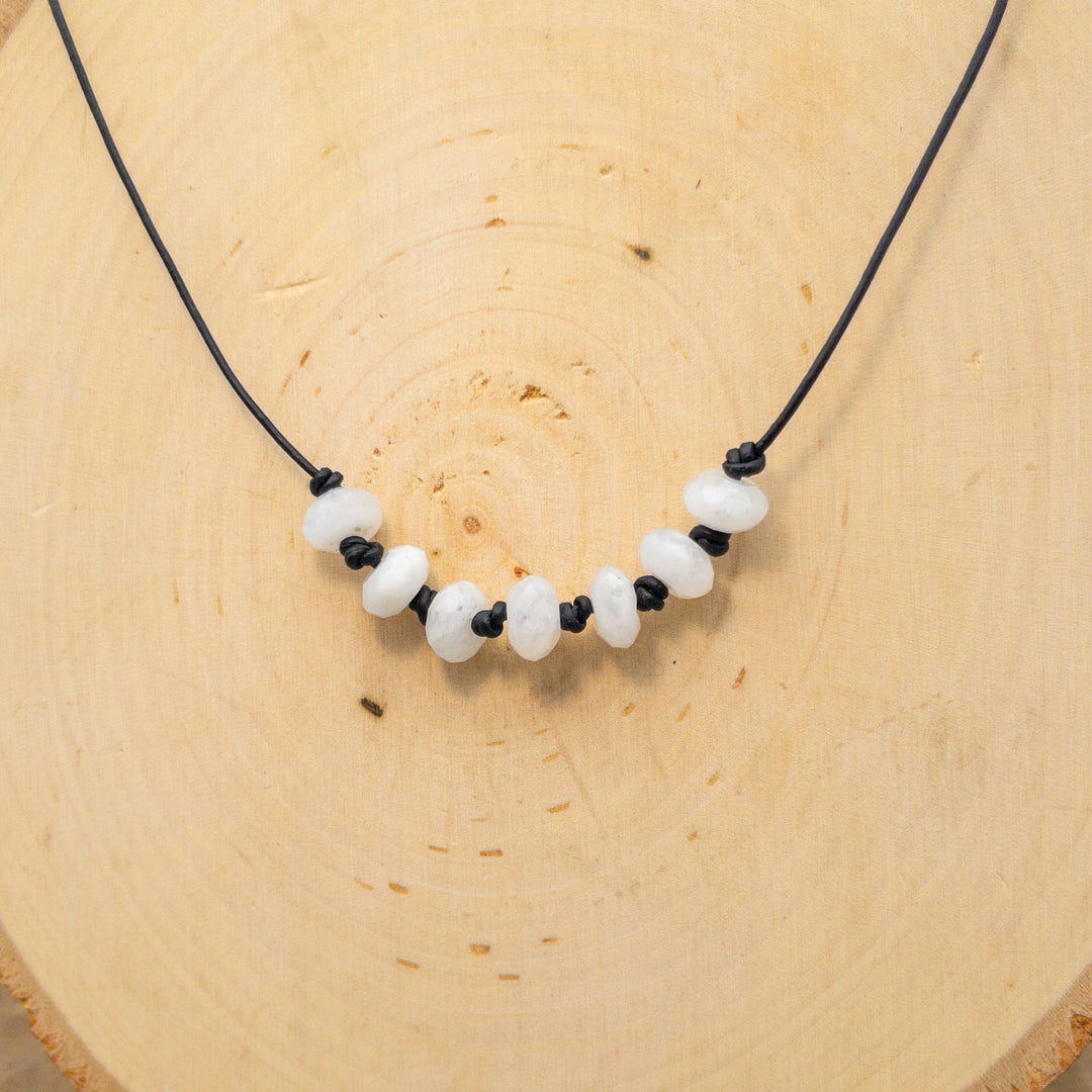 hand knotted rainbow moonstone beaded necklace on black leather with sterling silver clasp on wood background