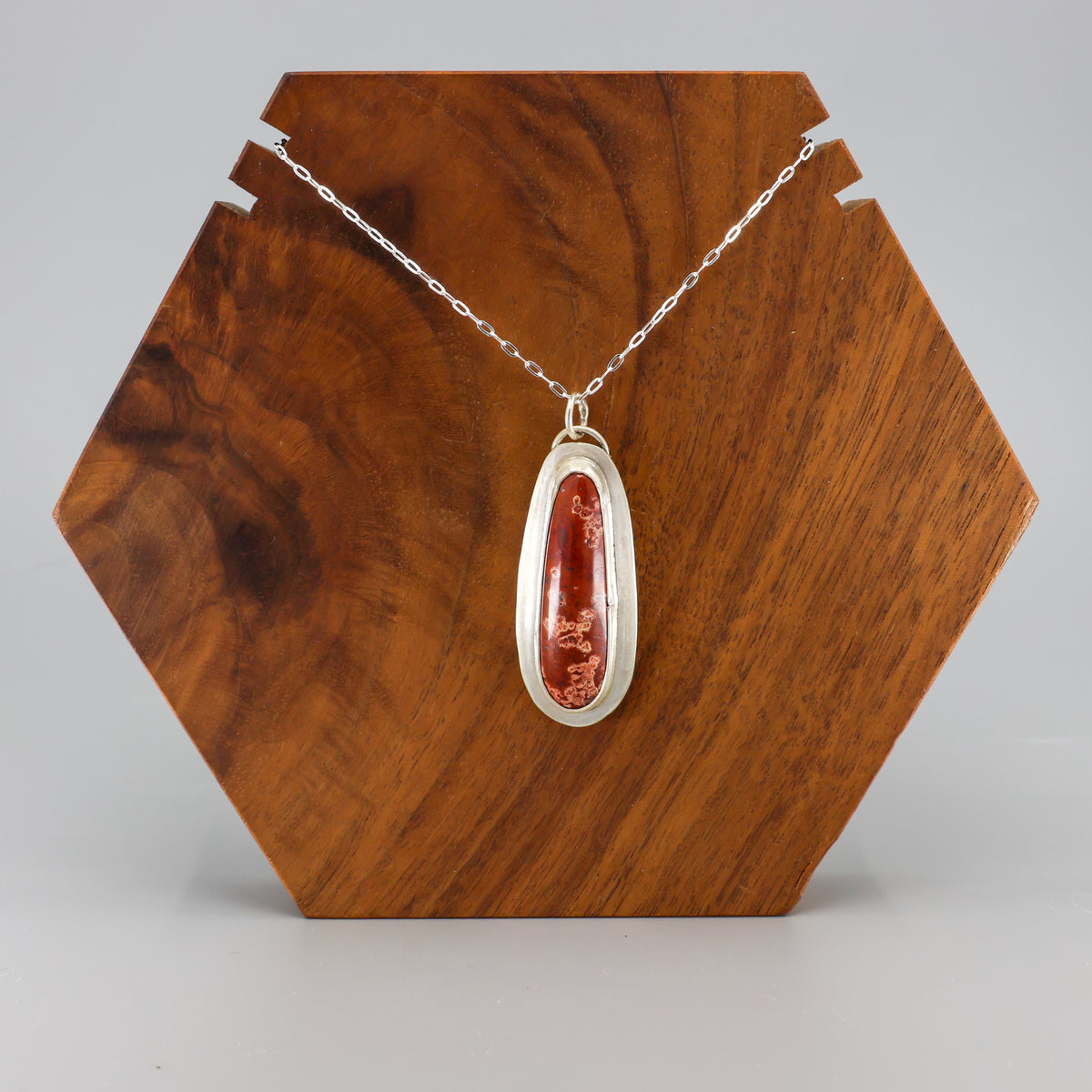 handmade red jasper sterling silver pendant on sterling silver chain on a wood block