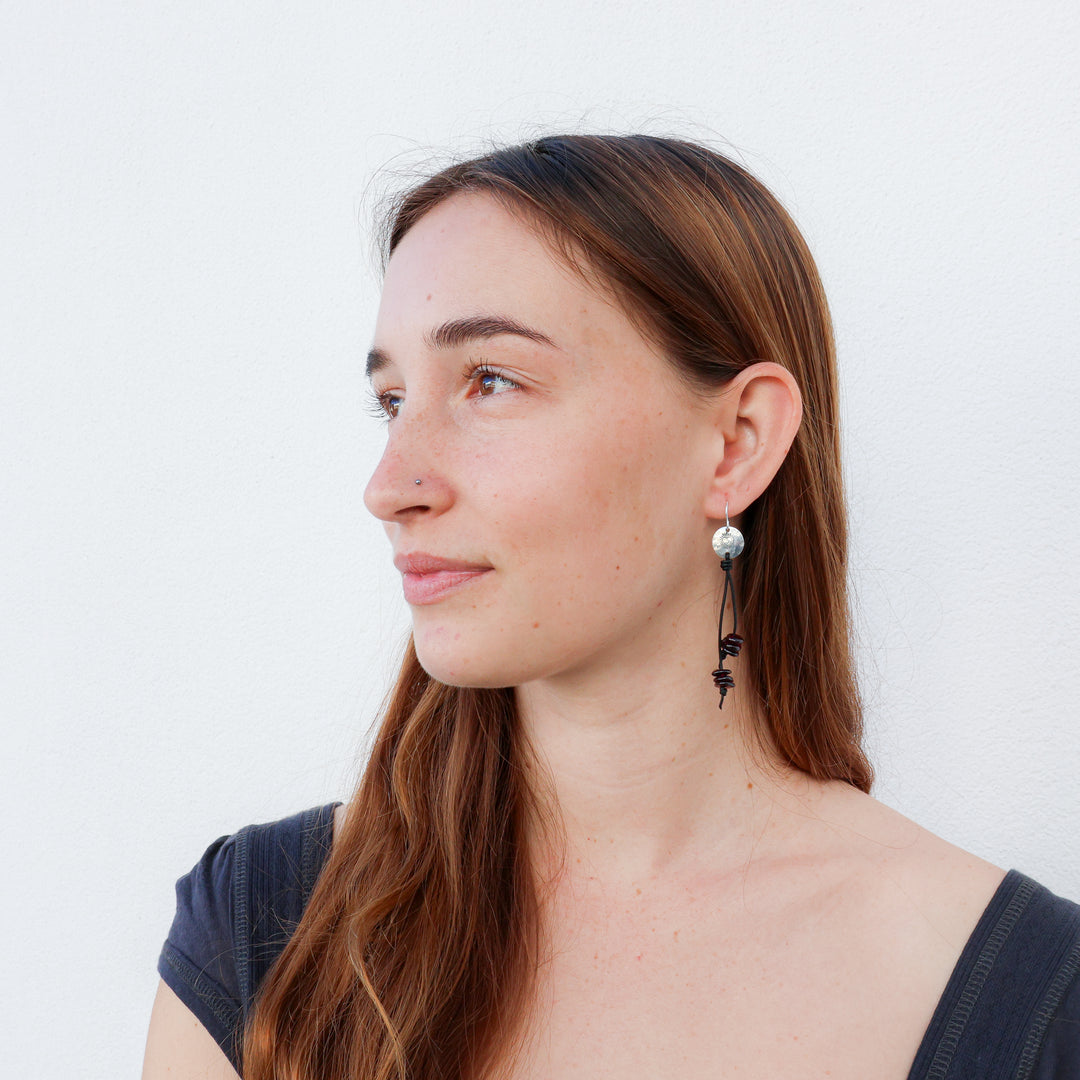 handmade earrings featuring heart stamped discs with garnet beads hanging from leather cords