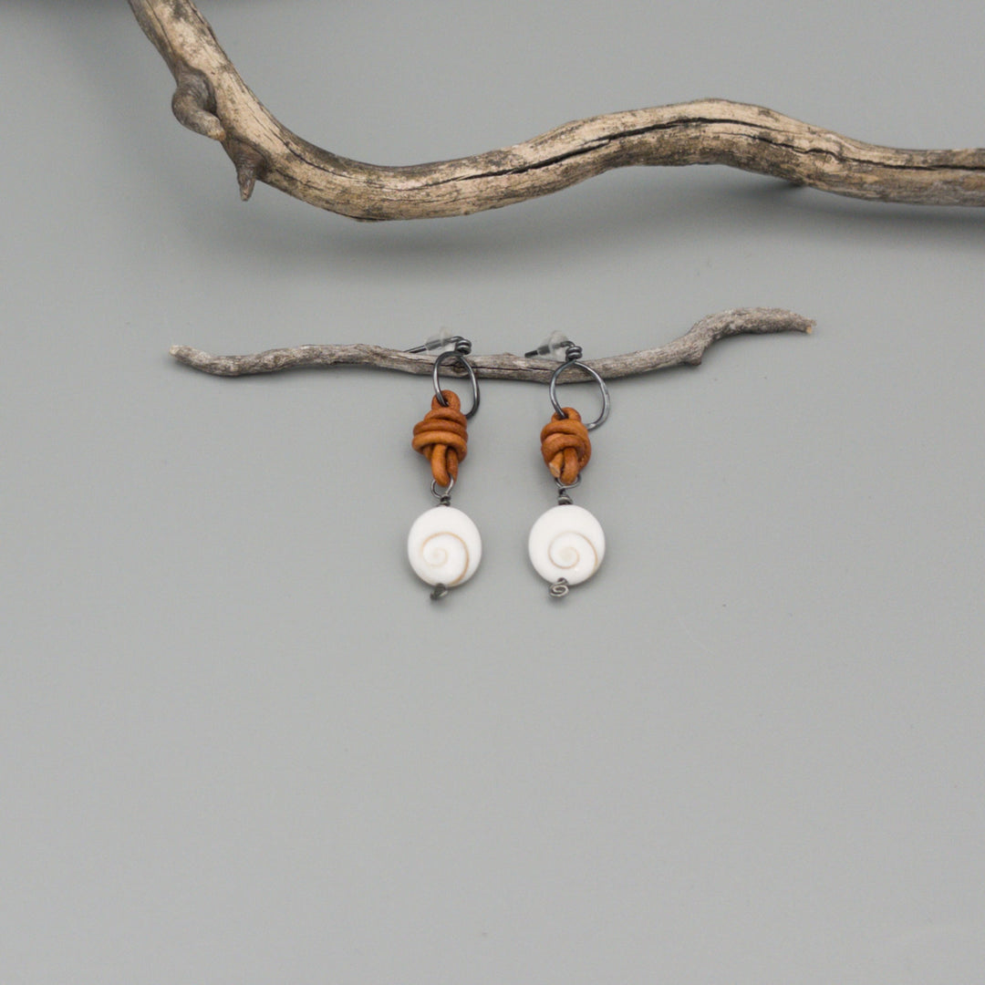 Shiva shell, leather, and oxidized sterling silver handmade earrings on a gray background