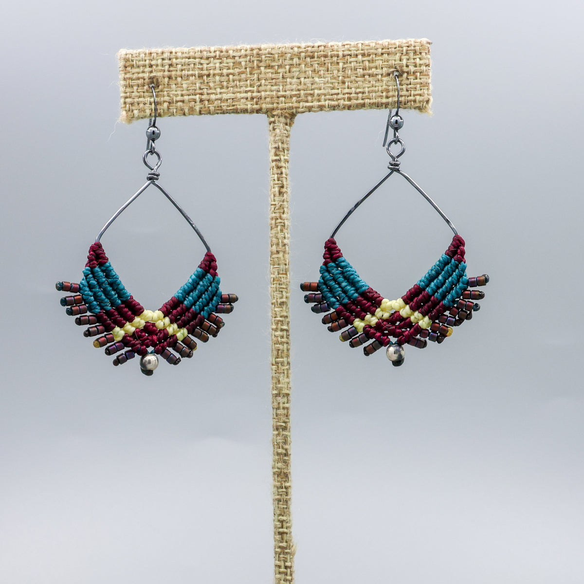 handmade square macrame hoop earrings oxidized sterling silver teal, deep burgundy, light yellow on a linen hanger