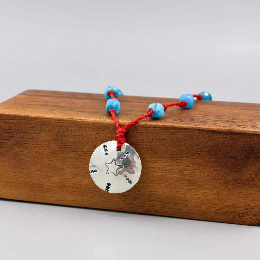 handmade silver stamped necklace with blue apatite beads on a red cord on a wood block