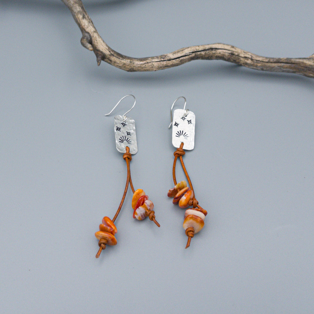 hand stamped sterling silver sunset spiny oyster and leather earrings on a gray background