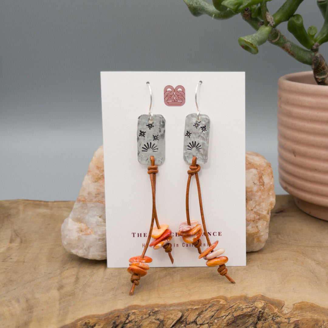 hand stamped sterling silver sunset spiny oyster and leather earrings on a white card