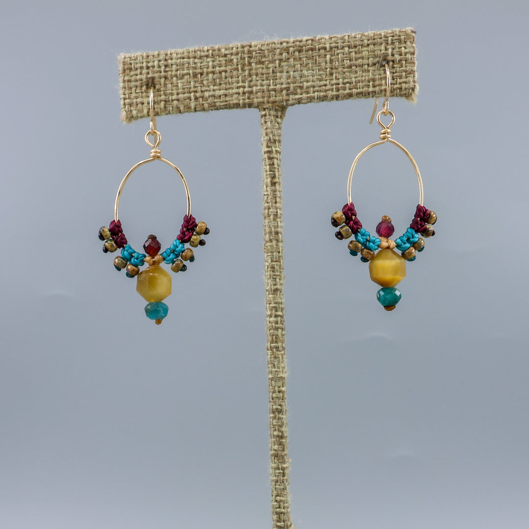 thunderbird inspired, 14k gold filled macrame hoop earrings with golden tiger's eye, blue apatite, and garnet beads on a linen hanger
