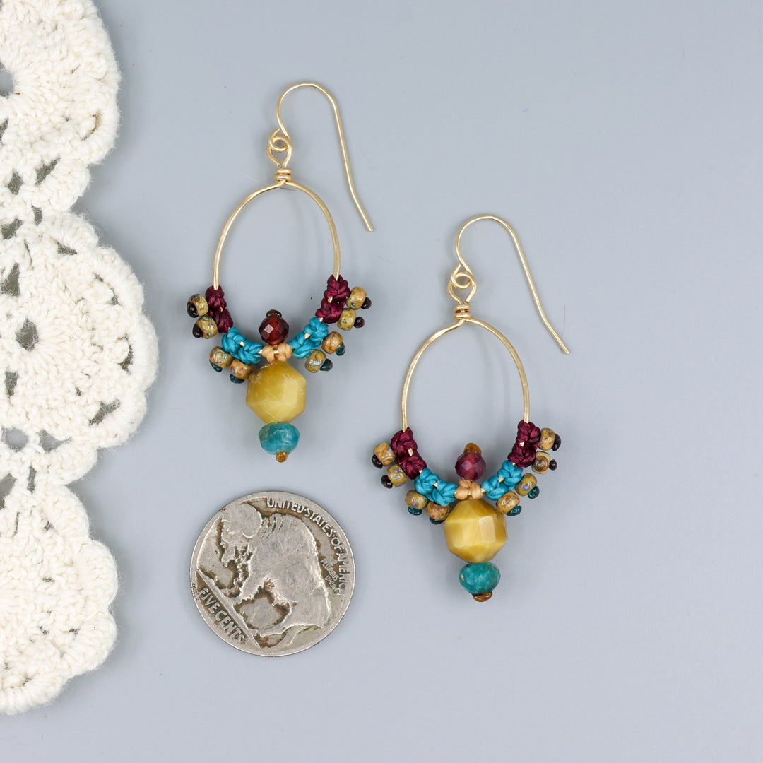 thunderbird inspired, 14k gold filled macrame hoop earrings with golden tiger's eye, blue apatite, and garnet beads with a nickel for size comparison