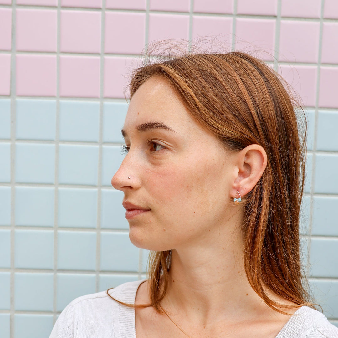 handmade, small triangle shaped gold macrame earrings with sunstone bead worn on a model