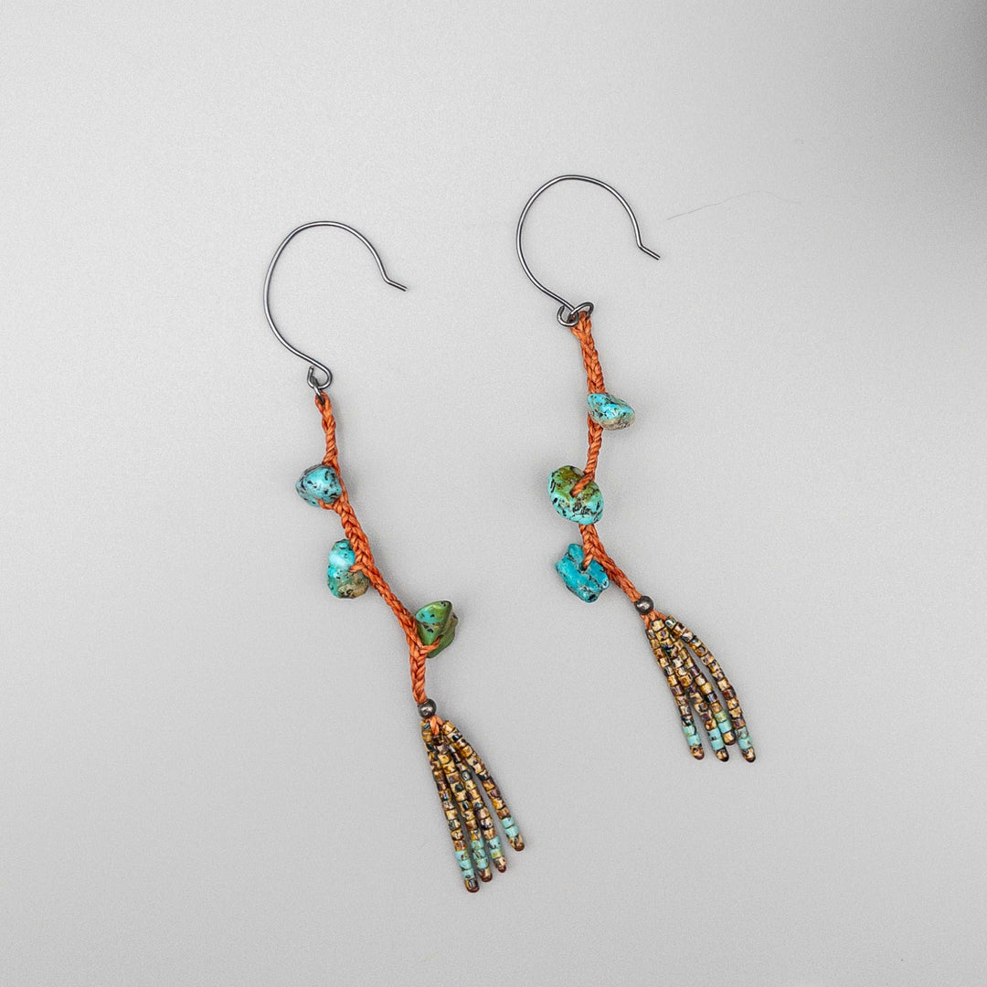 Turquoise dangle earrings with hand-formed oxidized sterling silver ear wires and a seed bead fringe on a gray background