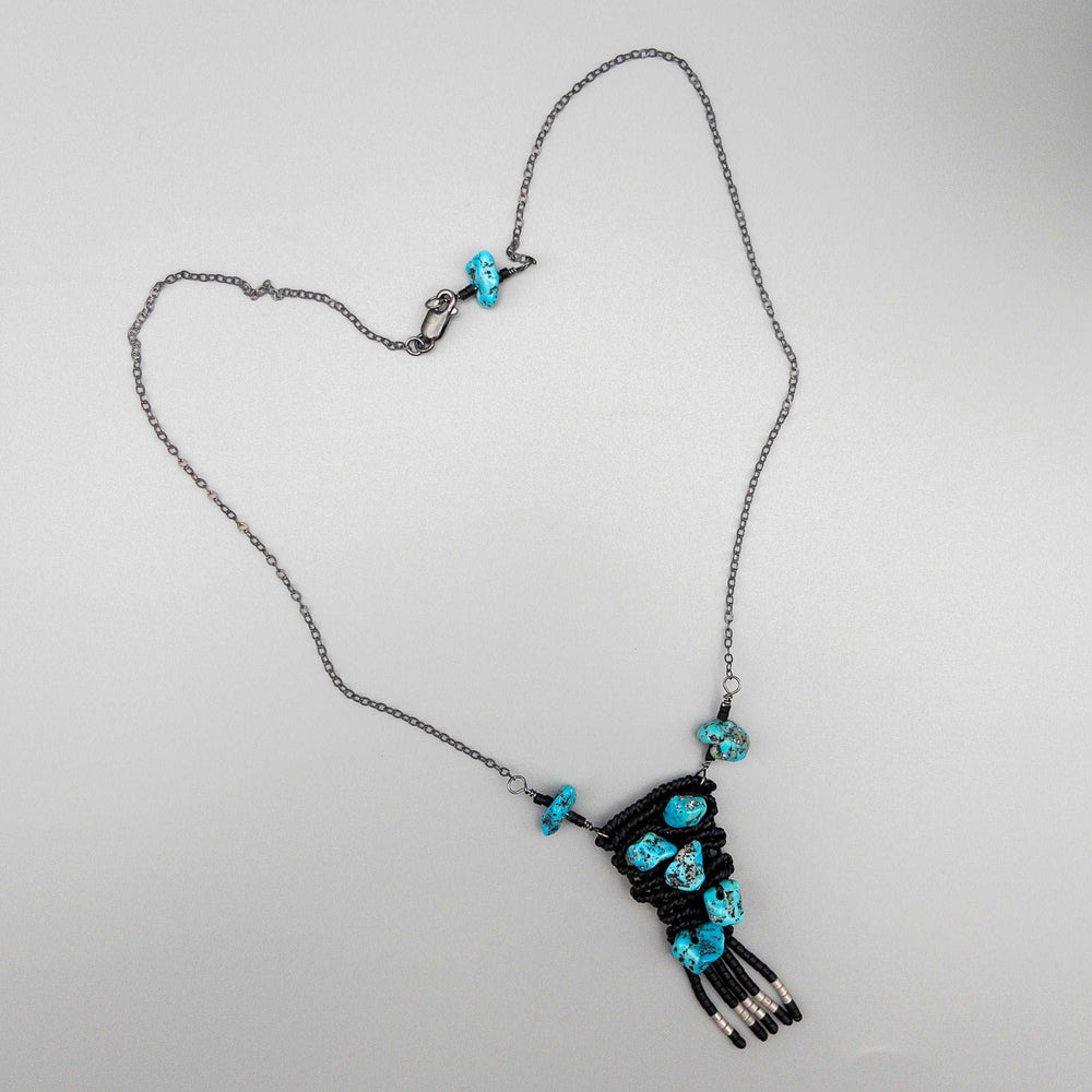 hand-woven macrame necklace with vintage kingman turquoise beads black with sterling silver chain shown flat on a gray background