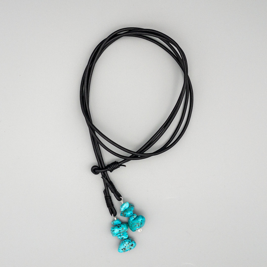 black leather western lariat necklace with turquoise beads shown on a gray background