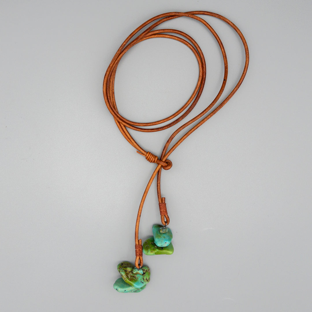 brown leather and turquoise western lariat style necklace on a gray background