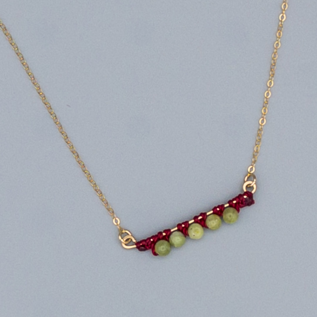 close up of 14k gold filled bar necklace with peridot beads and macrame