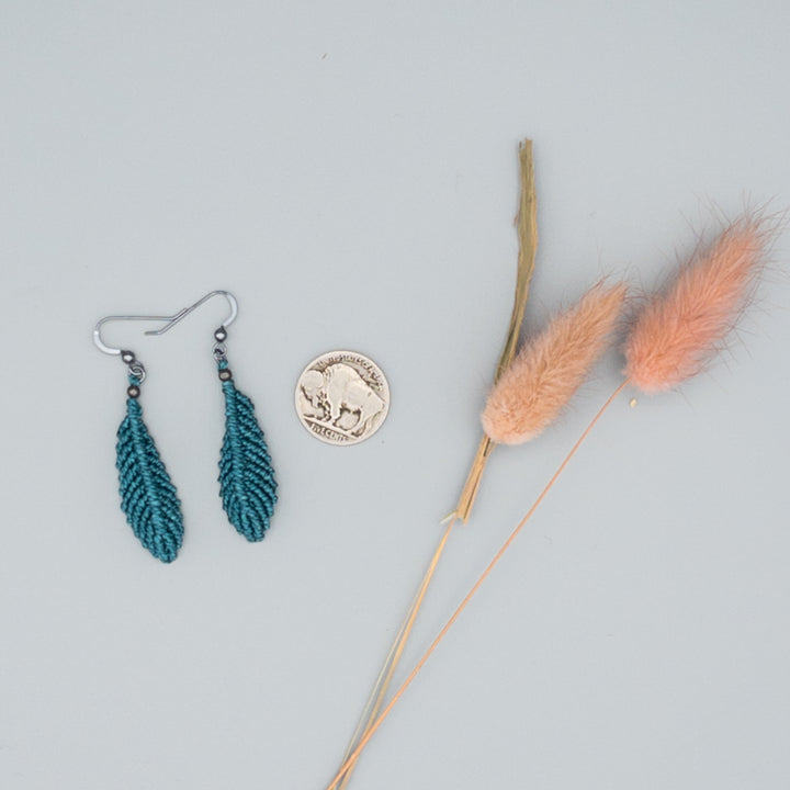Rich teal macrame feather earrings with oxidized sterling silver ear wires on gray background